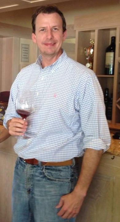 Sam Edelen holding a glass of red wine in a tasting room